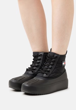 Bottines noires imperméables avec un dessus matelassé, bout rond, semelle épaisse et lacets avec accent de marque.
