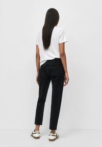 Černé džíny z denimu s vysokým pasem a rovnými nohavicemi, ve spojení s bílým tričkem s kulatým výstřihem a pohodlnými teniskami.