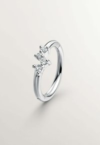 Anillo de plata con tres diamantes cortados en forma redonda en un engaste de garras, banda lisa con acabado pulido, diseño minimalista.