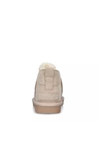 Stivaletti beige con materiale scamosciato morbido, fodera in lana e accenti laterali testurizzati. Presentano una suola piatta in gomma e un'etichetta sul retro con marchio.