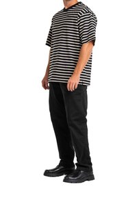 Černé a krémové pruhované tričko s krátkým rukávem, volný oversized střih, kombinované s černými kalhotami se zúženými nohavicemi a černými botami s masivní podešví.