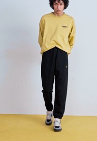 Yellow long-sleeve shirt with logo, paired with black sweatpants. Footwear features multi-colored accents and a chunky sole.