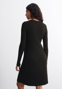 Abito nero a maglia a coste con maniche lunghe. Corpino aderente che si allarga in un orlo svasato, texture liscia. Design minimalista, senza chiusure visibili.