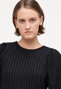 Black textured top with vertical ribbing, round neckline, and puffed sleeves. Fabric appears lightweight and slightly sheer.