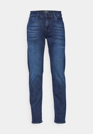 Jeans slim fit em denim azul escuro, com cinco bolsos, fecho de botão e detalhes costurados ao longo das costuras. Textura suave.