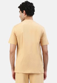 Kurzärmliges T-Shirt mit Rundhalsausschnitt aus hellem beigen Baumwollstoff. Glatte Textur mit einfachem Design. Keine sichtbaren Muster oder Logos.