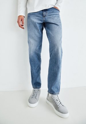 Lys blå denimjeans med rett passform, med subtil fading. Kombinert med grå semsket skinn sneakers med hvite såler og snøringer.