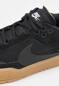 Black athletic shoe with textured fabric upper, suede accents, rubber sole, and raised Nike logo. Features lacing system and black stitching.