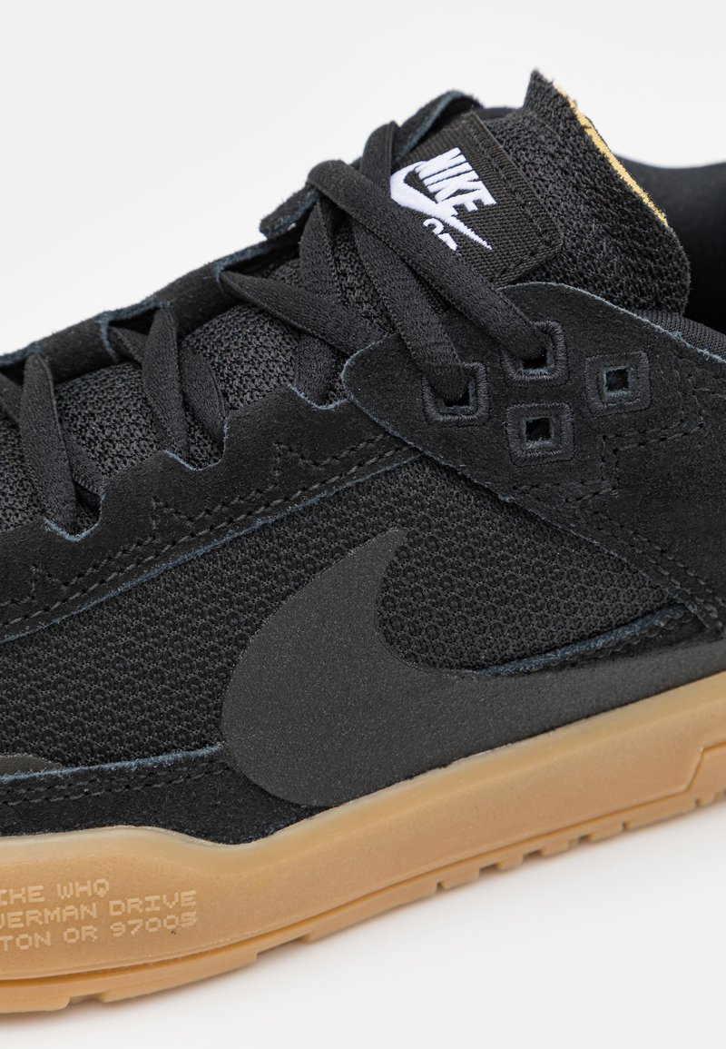 Chaussure de sport noire avec tige en tissu texturé, accents en daim, semelle en caoutchouc et logo Nike en relief. Comprend un système de laçage et des coutures noires.