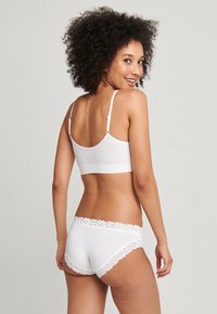 Vit bomullsbård med justerbara axelband, tillsammans med vita boyshorts med en spetstkant i midjan. Slät textur och åtsittande design.