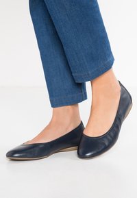 Marinblå läderballetskor med rund tå och slät yta, kombinerade med jeansbyxor, som visar en enkel design.