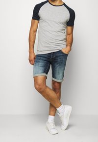 Camiseta gris de manga corta con mangas raglán en azul marino, combinada con pantalones cortos de mezclilla azul claro con dobladillos enrollados y zapatillas blancas.