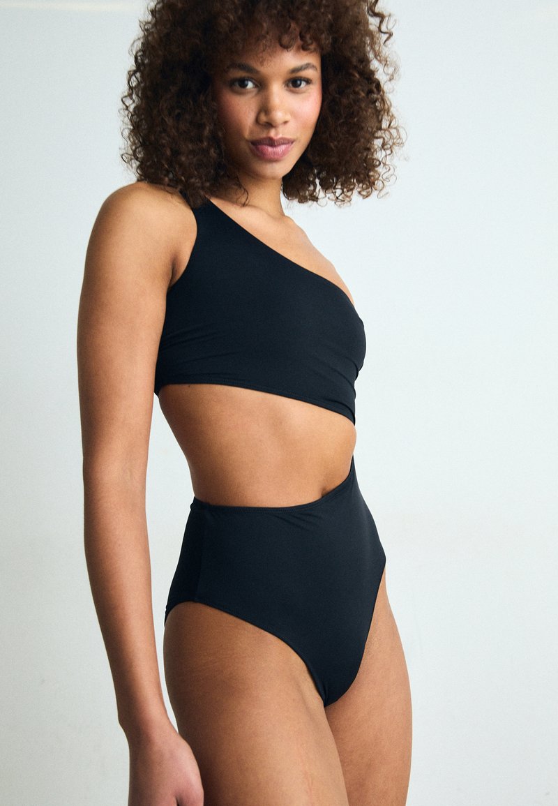 Svart en-skulder bikini topp kombinert med høyt liv-bikini underdel. Glatt tekstur, ensfarget, minimalistisk design, og ingen synlige mønstre.