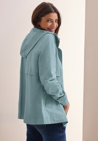 Hellblauer Kapuzenmantel aus glattem Stoff, mit Knopfleiste vorne und Seitentaschen. Das Design ist locker geschnitten mit einer leicht ausgestellten Silhouette.