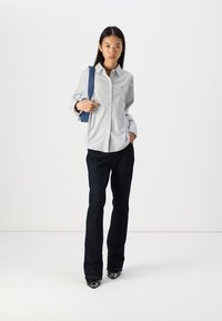 Camicia a righe blu e bianche con bottoni, abbinata a pantaloni flare in denim scuro e tacchi neri, indossata con una borsa a tracolla blu.