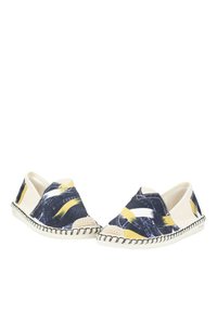 Las zapatillas slip-on de lona presentan un patrón abstracto en azul marino y blanco con acentos amarillos. La suela de yute trenzado aporta textura y contraste.