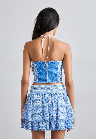 Modrý a biely vzorovaný crop top s halter krkom a zipsom na chrbte, doplnený o poschodovú mini sukňu so podobnými vzormi a elastickým pásom.