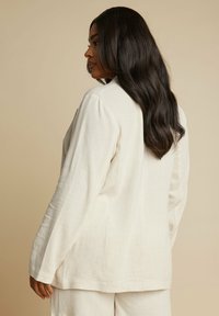 Linneblazer i ljusbeige med avslappnad passform, långa ärmar och subtil textur. Designad med notched krage och ryggslits för ökad rörelsefrihet.