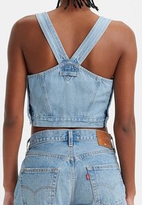 Ljusblå denimcrop topp med vida axelband, en V-formad rygg och rå kant. Tyget har en blekt textur som kompletterar matchande denimjeans.