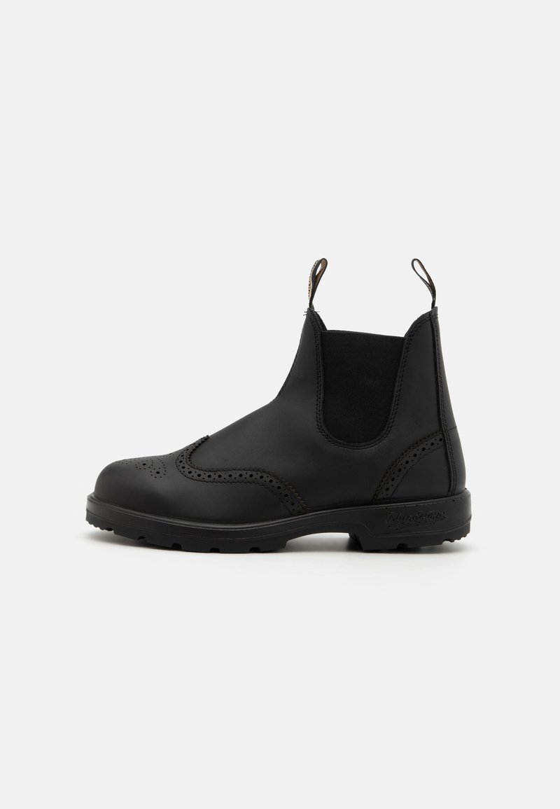 Botas de tornozelo em pele preta com painéis laterais elásticos, detalhes brogue, alças de puxar e uma sola de borracha texturizada.