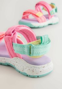 Sandaaltjes voor kinderen met roze en mintkleurige bandjes, zachte paarse en gele binnenzolen, en wit gespikkelde zolen; voorzien van verstelbare bandjes.