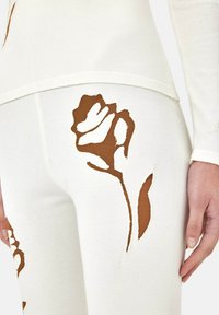 Witte gebreide leggings met bruine rozenprint in verschillende maten. Opvallende uitsnijdingen verbeteren het ontwerp en creëren visuele textuur.