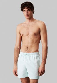 Costume da bagno azzurro chiaro realizzato in tessuto liscio e ad asciugatura rapida, con vita elasticizzata, cordino e logo stampato su un lato.