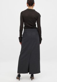 Mørkegrå, ankel-lang nederdel med en lige silhuet, sideslids og minimal dekoration. Bæres med en tætsiddende bluse med lange ærmer.