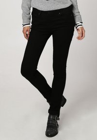 Jean noir skinny avec une texture lisse, doté d'un design classique à cinq poches, associé à des bottines ornées de clous.