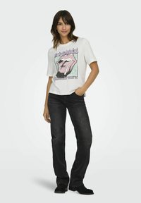 Hvid bomulds t-shirt med et Rolling Stones grafik i pink og blå, parret med sorte denim jeans og sorte ankelstøvler.