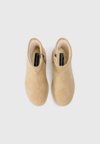 Bottines en daim beige avec une texture lisse, dotées d'une fermeture éclair, d'une doublure intérieure douce et d'un design à bout arrondi.