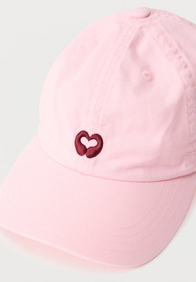 Ανοιχτό ροζ καπέλο μπέιζμπολ με ένα μικρό κεντητό μαρουαν καρδιά στο κέντρο μπροστά, γωνιασμένο ώστε να φαίνονται οι λεπτομέρειες της ραφής.