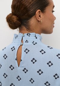 Blusa azzurro chiaro con finitura texturizzata, caratterizzata da una fantasia floreale nera, colletto arricciato e un piccolo foro a chiave sul retro con bottoni.