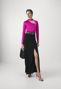 Top fucsia a maniche lunghe con design a taglio abbinato a una gonna maxi nera con cintura e spacco laterale. Gli accessori includono una borsa nera e tacchi a fascia.