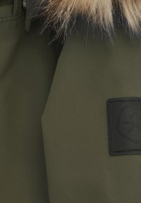 Zielony materiał wierzchni z wykończeniem teksturowanym, z sztucznym futrem przy kołnierzu oraz czarną gumową naszywką z logo.