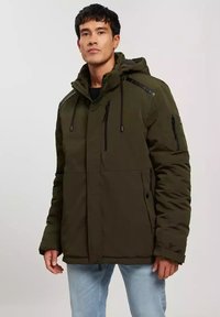 Oliwkowa izolowana kurtka z zapięciem na zamek błyskawiczny, regulowanym kapturem i czarnymi akcentami. Posiada wiele kieszeni zapinanych na zamek oraz pikowaną fakturę.