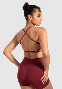 Bordeaux sport-bh met kruislings gespen en metalen hardware, gecombineerd met hoge taille shorts in dezelfde stof, die een gladde textuur laat zien.