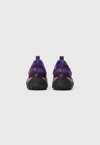 Sneakers with a mesh upper in maroon and blue, featuring a textured black rubber sole and contrasting "FUTURE VERSACE" branding on the heel.