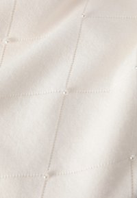 Fehér szövet, puha tapintással, steppelt mintával és kis gyöngyökkel a varrások találkozásainál.