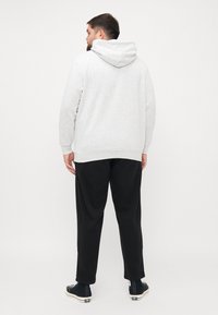 Grå hættetrøje med en afslappet pasform, parret med sorte bukser og sorte sneakers. Stoffet ser blødt og struktureret ud.
