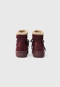 Stivali alla caviglia in suede bordeaux con una morbida fodera beige, chiusura con lacci e suola in gomma con dettagli del marchio in rilievo sul tacco.