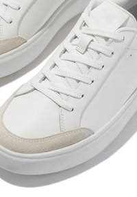 Weißer Low-Top-Sneaker mit dicker Sohle, weißen Schnürsenkeln und beigem Wildlederschnitt im Zehenbereich, teilweise von oben sichtbar.