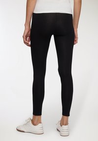 Czarne legginsy wykonane z gładkiego, elastycznego materiału. Dopasowany krój z wysokim stanem, zestawione z białymi butami sportowymi.