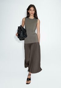 Olivgrünes ärmelloses Oberteil kombiniert mit braunen plissierten Hosen, getragen mit schwarzen Riemchensandalen und einer schwarzen Handtasche.