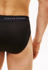 Schwarze Baumwollschlüpfer mit elastischem Bund, der das Logo "TOMMY HILFIGER" in Weiß zeigt. Glatte Textur und enger Sitz, konzipiert für Komfort.