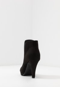 Stivale alla caviglia in suede nero con tacco, punta arrotondata, tacco affusolato e cuciture minime, caratterizzato da una superficie liscia e un'apertura con zip sul retro.
