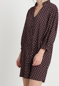 Black dress with red floral pattern, long sleeves, button-down front, relaxed fit, and collar. Made from lightweight fabric with a smooth texture.