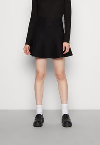 Falda negra acampanada hecha de tela suave, combinada con un top ajustado de manga larga, calcetines blancos y zapatos negros gruesos.