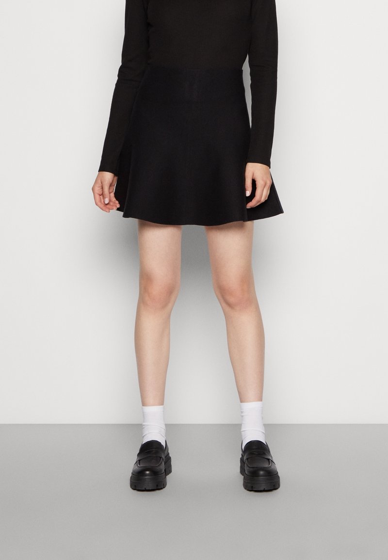 Falda negra acampanada hecha de tela suave, combinada con un top ajustado de manga larga, calcetines blancos y zapatos negros gruesos.
