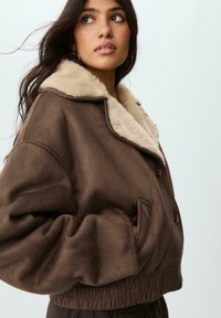 Giacca in finta suede marrone con colletto in finta pelliccia beige, maniche voluminose, vita a coste e chiusura frontale con bottoni.